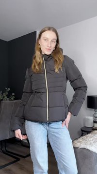 Μαύρο μπουφάν puffer με φερμουάρ μπροστά, καπιτονέ σχέδιο και τσέπες. Συνδυασμένο με ανοιχτό μπλε τζιν σε σύγχρονο εσωτερικό χώρο.