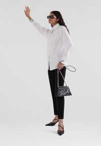 White button-up shirt, black fitted pants, black pointed flats, and a black leather handbag with chain strap and white signature logo detail.