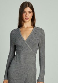 Rochie gri din material texturat, cu mâneci lungi, cu dungi verticale și detalii subtile. Decupaj în V și talie ajustată.