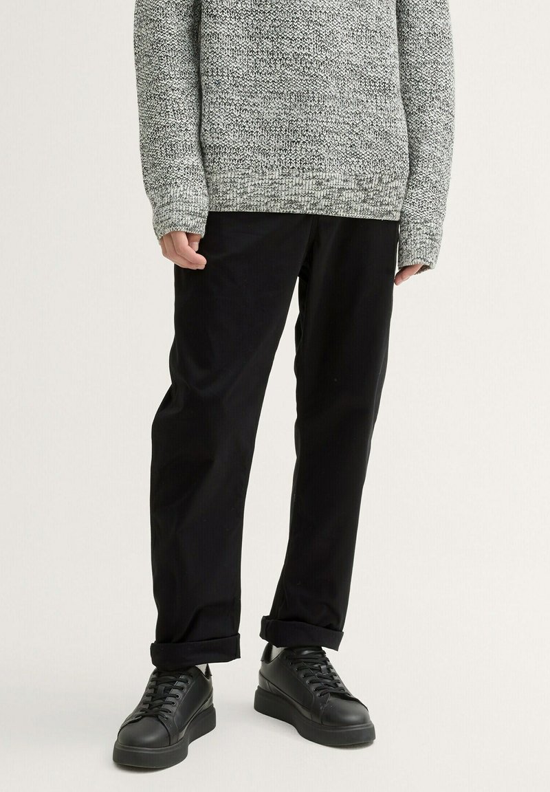 Pantalones de algodón negro con un corte holgado, con puños enrollados, combinados con zapatillas negras elegantes y un suéter gris texturizado.