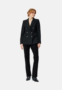 Blazer double boutonné noir avec des boutons en argent, revers pointus et deux poches, associé à un pantalon noir ajusté et des bottes à talons.