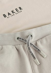 Světle béžová mikina s vyraženým logem "BAKER by TED BAKER". Obsahuje žebrovaný límec a šňůrku s logem na koncích.