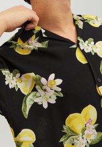 Camicia a maniche corte in tessuto nero con un vivace motivo di limoni e fiori, dotata di colletto classico e chiusura a bottoni.
