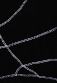 Svart tyg med framträdande vit sömnad i korsande, abstrakta mönster. Slät textur med synliga sömmar och sömnadsdetaljer.