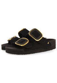 Sandalias negras con dos correas anchas y hebillas doradas cuadradas y texturizadas. Superficie suave, suela plana y textura en la parte inferior similar al caucho.