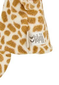 Soft plush fabric with brown and white giraffe spots and a sewn-in CE compliance label showing manufacturer details.