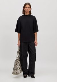 Zwarte oversized t-shirt met korte mouwen, gecombineerd met losse zwarte cargobroeken en een tas met een zebra-print patroon.
