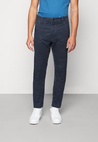 Mörkblå bomullschinos med slim passform, med en framknappsstängning, bälteshällor och sidofickor, kombinerat med vita sneakers.