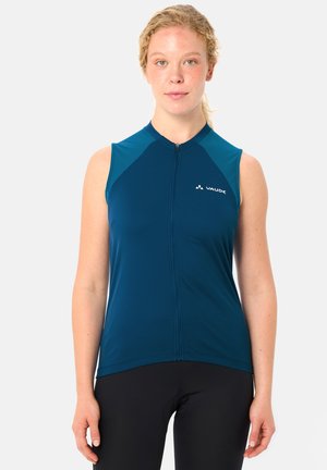 Frau mit lockigem blondem Haar, die ein ärmelloses blaues Radtrikot mit Frontreißverschluss und schwarze Radhosen trägt, nach vorne blickend.