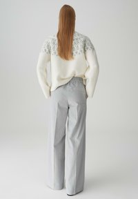 Maglione bianco con la parte superiore grigia a motivo, abbinato a pantaloni grigi chiari a gamba larga con vita elastica. Tessuti morbidi, vestibilità casual.
