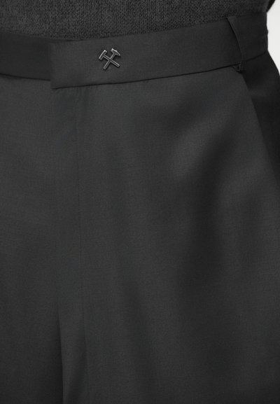 Juodos pritaikytos kelnės su lygiomis tekstūromis, turinčios plokščią juosmenį ir subtilų juodą logotipą, pabrėžiančios elegantišką dizainą.