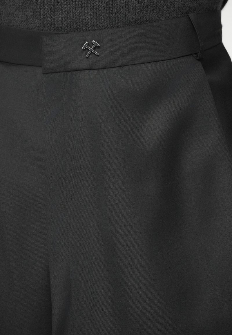 Pantalones negros ajustados con una textura suave, cuentan con una cinturilla plana y un sutil acento de logo en negro, enfatizando un diseño elegante.