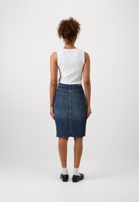 Saia de ganga em azul escuro com uma silhueta ajustada, de comprimento médio e bolsos traseiros. Combinada com uma blusa branca sem mangas e sapatos pretos.