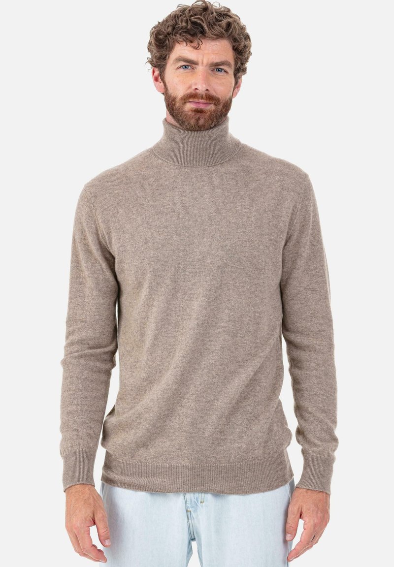 Pull-over à col roulé marron en matière douce avec une coupe ajustée, poignets et bordures côtelés. Porté avec un jean bleu clair.