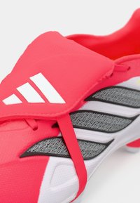 Ποδοσφαιρικό παπούτσι Adidas σε φωτεινό ροζ και λευκό, με υφή στην επάνω επιφάνεια, γκρι λεπτομέρειες και ασφαλή λουρί για άνετη εφαρμογή και υποστήριξη.