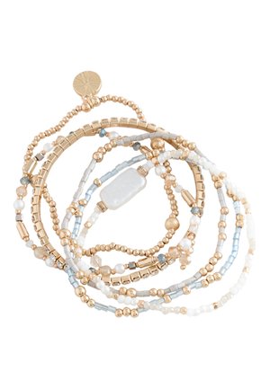 Stack of gold, white, and blue beaded bracelets with various bead shapes and a round gold charm on a white background.