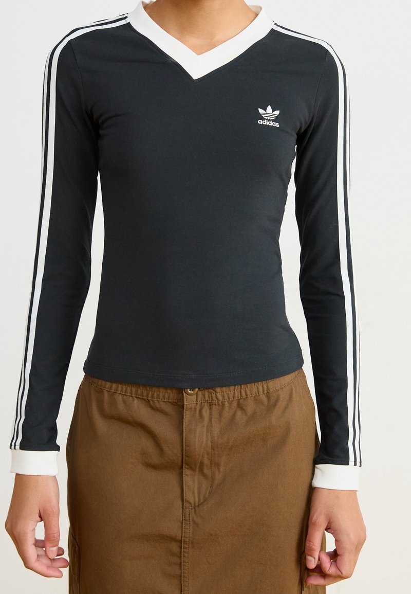 Černá dlouhá rukávová košile s bílým výstřihem do V, logem Adidas a bílými pruhy na rukávech; výrazný střih a hladká textura.