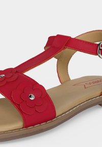 Κόκκινο επίπεδο σανδάλι με λουράκι στον αστράγαλο, κλείσιμο με πόρπη και διακοσμητικές στρωματοποιημένες ανθισμένες λεπτομέρειες στο εμπρός λουράκι.