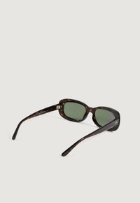 Gafas de sol rectangulares de carey con lentes verdes y patillas delgadas, descansando abiertas sobre un fondo claro.