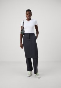 White short-sleeve shirt with red detail, dark grey pencil skirt, and black pants paired with white sneakers featuring green laces.