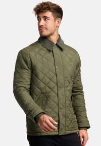 Grøn quilted jakke med trykknaplukning, prydet med en fløjlskrave og sidelommer, lavet af et let, polstret materiale.
