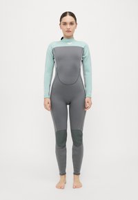 Peldkostīms ar pelēku ķermeni, gaiši ziliem piedurknēm, ceļgalu aizsargiem un augstu apkakli. Izgatavots no neoprēna ar gludu, teksturētu apdari.