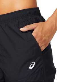 Zwarte sportshorts met een elastische tailleband, zijzakken en een wit logo. De stof lijkt glad en lichtgewicht.