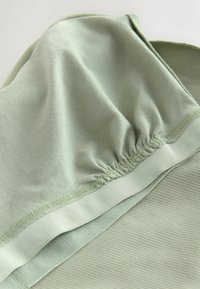 Gros plan sur un tissu doux vert clair avec une couture élastique froncée et une texture côtelée sur un vêtement.