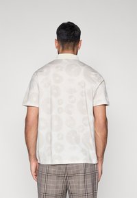 Trumpomis rankovėmis, apykakle, šviesiai balta marškiniai su subtiliu gėlių raštu. Pagaminti iš lengvos medžiagos, turi klasikinį kirpimą ir minkštą tekstūrą.