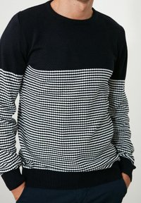 Kreuzkragenpullover aus marineblauem und weißem Garn. Verfügt über einen strukturierten schwarzen oberen Abschnitt, ein horizontales Streifenmuster im unteren Teil und gerippte Bündchen.