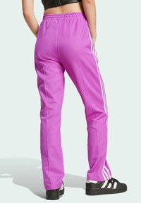 Rosa träningsbyxor med en avsmalnande passform, med vita sidostreifen, elastisk midja och ribbad textur. Svarta sneakers synliga.