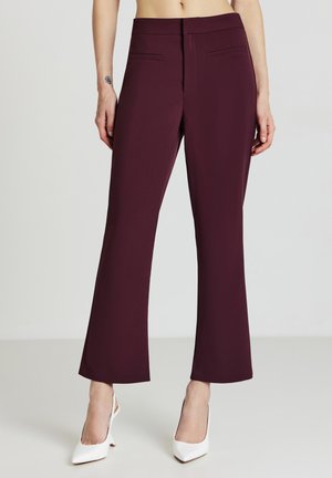 Pantaloni svasati color bordeaux con una trama liscia, dotati di tasche frontali e una vestibilità sartoriale, abbinati a décolleté bianchi a punta.