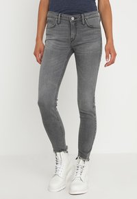Jeans skinny de denim gris con cintura alta, que presentan un dobladillo deshilachado y un diseño de cinco bolsillos, combinados con botas blancas con cordones.