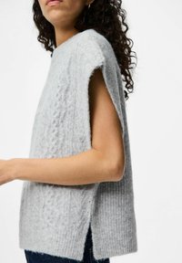 Ljusgrå stickad tröja med lös passform, korta ärmar, sidoklyftor och ett strukturerat mönster på tyget. Mjuk material.