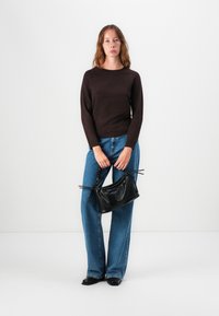 Brun genser, blå vide jeans og en liten svart strukturert håndveske med snøring. Enkle sorte sko fullfører antrekket.
