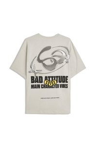 Světle šedé oversized tričko s lesklým designem, na kterém je nápis "BAD ATTITUDE" a "MAIN CHARACTER VIBES" v černé a žluté barvě.