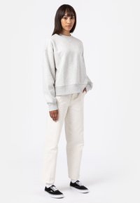 Felpa grigia, con texture, a collo rotondo, abbinata a pantaloni bianchi a gamba dritta e sneakers nere con lacci e suole bianche.