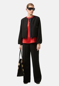 Sort bomberjakke med lynlås, rød top, sorte bukser med vide ben og en sort og beige stribet shopper. Tilbehør inkluderer store solbriller.