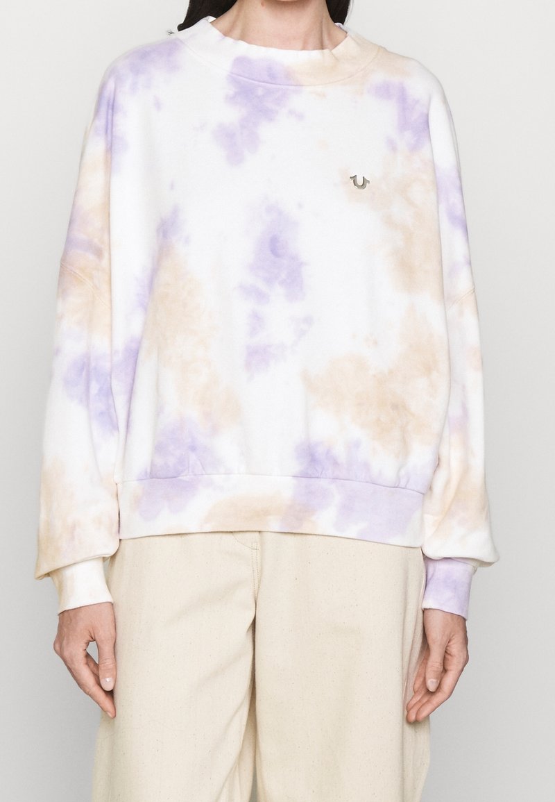 Vit tie-dye sweatshirt med lavendel- och beige mönster, rund halsringning och ribbade ärmslut, med en diskret logga på bröstet.