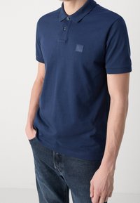 Námořnické modré polo tričko vyrobené z bavlny, s klasickým límečkem, dvouknoflíkovým zapínáním a malou logem na levé hrudi.