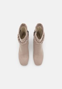 Bottines beige clair avec une texture en daim lisse, présentant un accent tressé et des zips sur le côté pour la fermeture. Conception à bout rond.