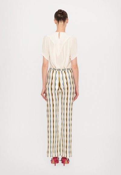 Krämfärgad blus med nyckelhålsöppning i ryggen och korta ärmar, kombinerad med flerfärgade randiga vida byxor. Klara röda klackar kompletterar outfiten.
