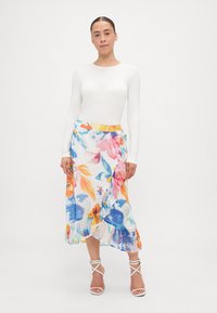 Jupe maxi florale avec un ourlet à volants, fabriquée en tissu léger. Présente des couleurs vives : rose, bleu, orange et vert sur un fond blanc.