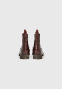 Bottes chevilles en cuir marron avec un motif serpent texturé, zips latéraux et languettes de tirage. Semelles épaisses avec un motif pour une meilleure adhérence.