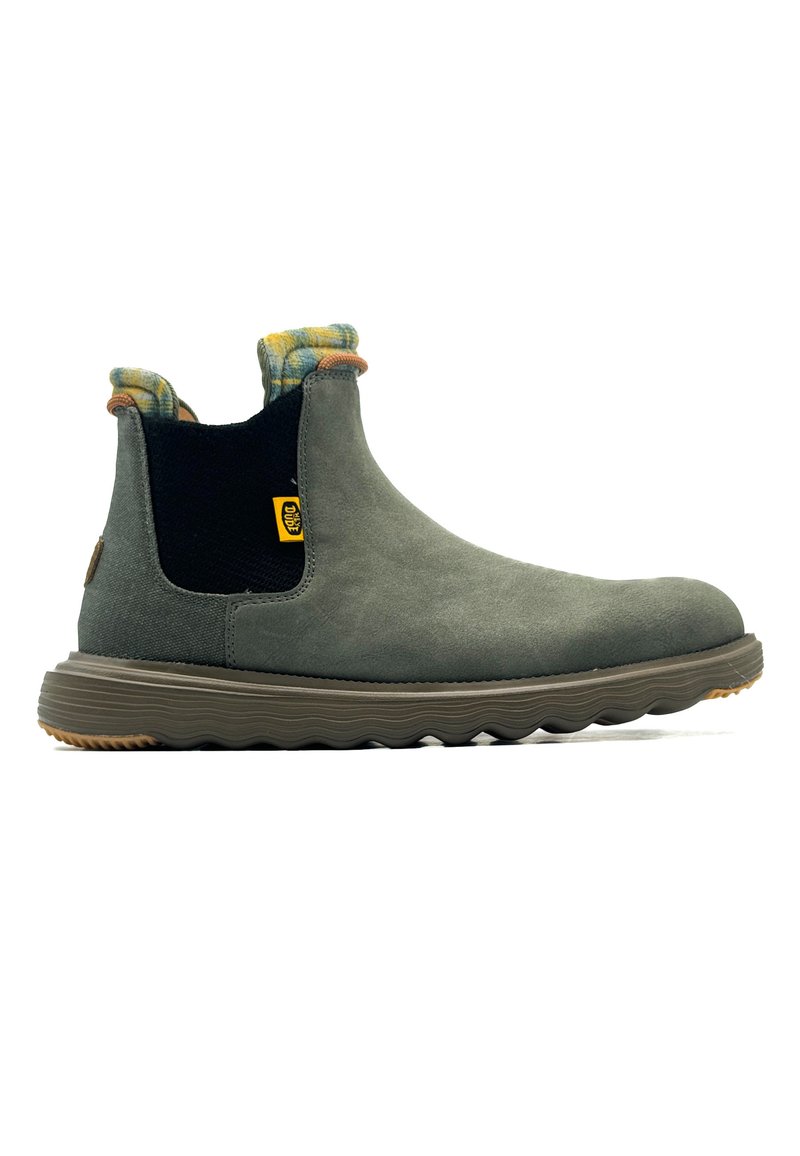 Botín Chelsea de ante gris con un panel lateral elástico negro, detalle de cuadro amarillo y azul en el cuello, y una suela de goma texturizada.