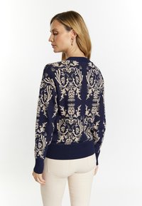 Maglione navy con motivo floreale crema, polsini e orlo a costine, texture lavorata a maglia, vista posteriore, maniche lunghe, vestibilità leggermente rilassata.