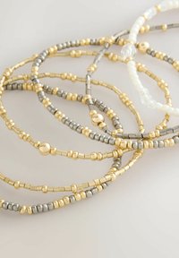 Gold- und silberne Perlenarmbänder zeigen eine Mischung aus runden und zylindrischen Perlen mit glänzender Oberfläche und verflochtenen Designs.