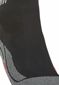 Calcetín deportivo negro con un patrón de tejido texturizado, que presenta acentos grises y detalles rojos. Incluye refuerzos en las áreas del talón y los dedos.