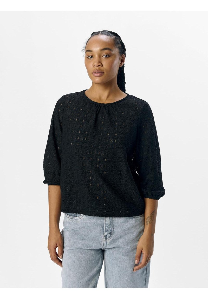 Black, lacy top with three-quarter sleeves and a round neckline. Features a textured pattern with a loose fit. Paired with light blue jeans.
