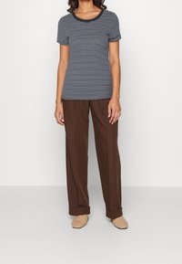 Marinblå och vit randig t-shirt med rundhals, matchad med löst sittande bruna byxor och neutrala slip-on-skor.